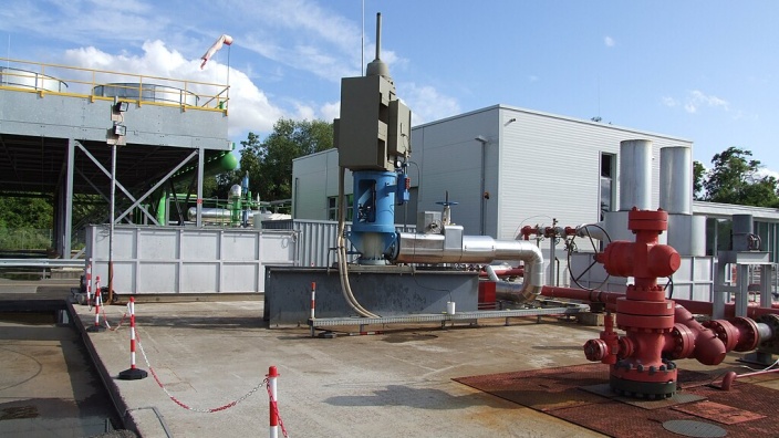 Förderbohrung und Reinjektionsbohrung des Geothermiekraftwerks Landau. Blau in der Mitte die Förderbohrung mit der Gestängepumpe, rechts rot die Reinjektionsbohrung, hinten mitte das Pumpenhaus für die Reinjektion, links ein Teil der Trockenkühlung